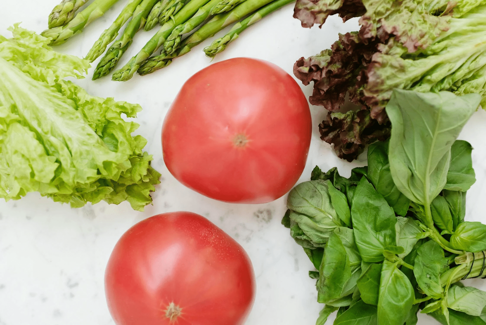 tomatoes, lettuce, spinach, and asparagus laying on a table