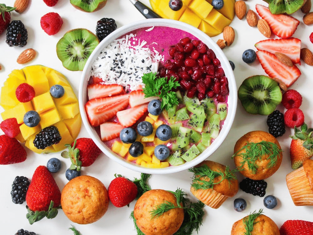 bowl filled with fruit and yogurt with fruits surrounding bowl on table